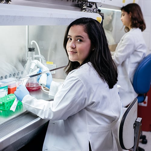 Student using a pipette in the lab and looking at the camera.