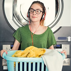 Student wearing headphones and holding a laundry basket in a laundry room.