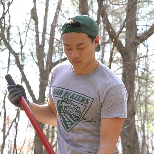 Student in UAB shirt outside holding a rake.