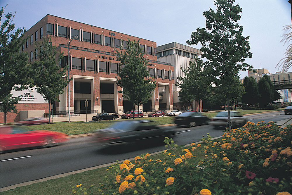 Exterior of the Lister Hill Library with trees and blurred cars in the foreground. 