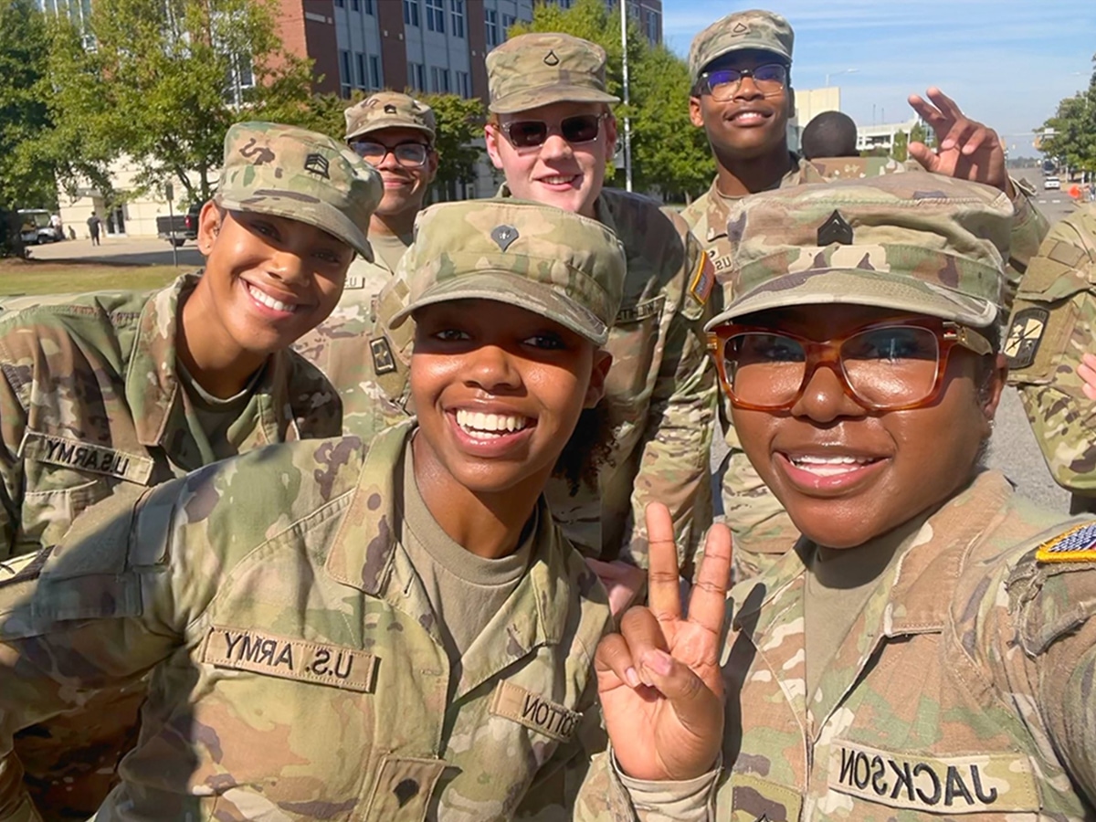 A diverse group of trainees in camo pose smiling at the camera.