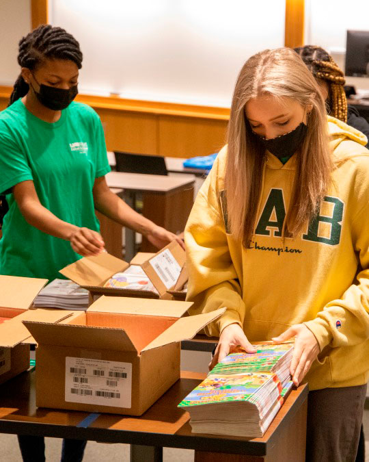 Two scholars in facemasks sorting donated books. 