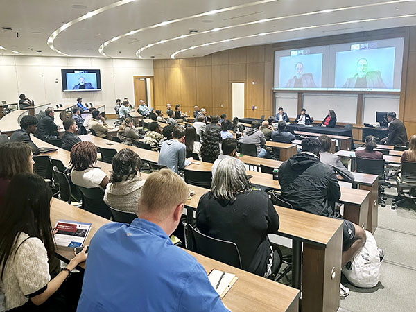 Students seated and listening to three panelists in front of an auditorium