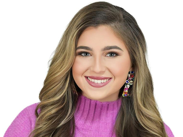 Headshot of a smiling student with long, wavy hair wearing a bright pink mock turtleneck sweater