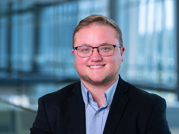 Headshot of a smiling person with short hair and glasses in a dark suit