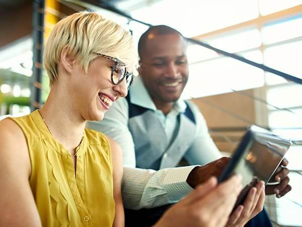 Female professional and male colleague smile while looking at iPad.