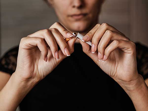 Unrecognizable young woman breaking a cigarette in half to stop smoking. Concept of smoking and addiction.