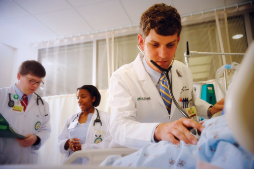 Dr. Jody Hughes (Pulmonary, Allergy, and Critical Care) examining unidentified patient in hospital room; two unidentified residents are in background, 2011.