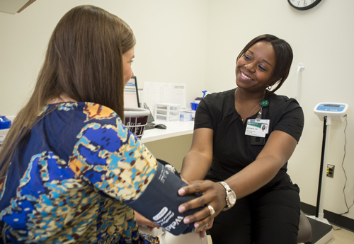 UAB Medicine Urgent Care Clinic, 2014. From side, African-American nurse is taking blood pressure for female patient in examination room, 2014.