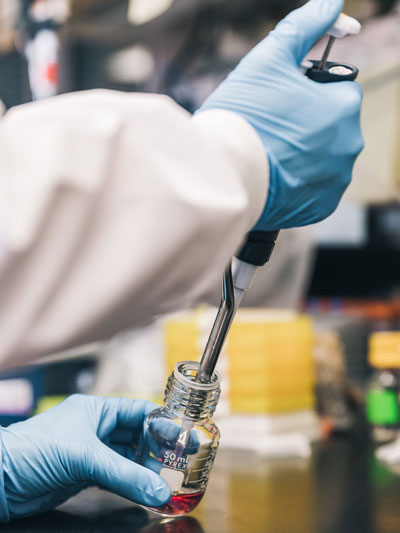 Scientist in lab gloves extracting material from a glass bottle.