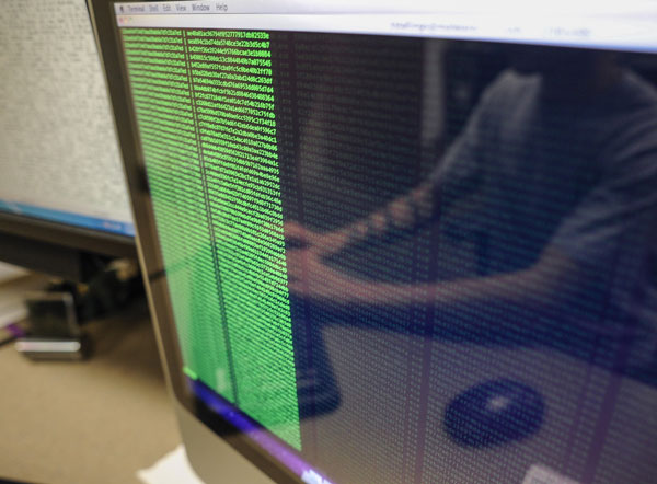 The reflection of a student can be seen on a computer screen full of code. 