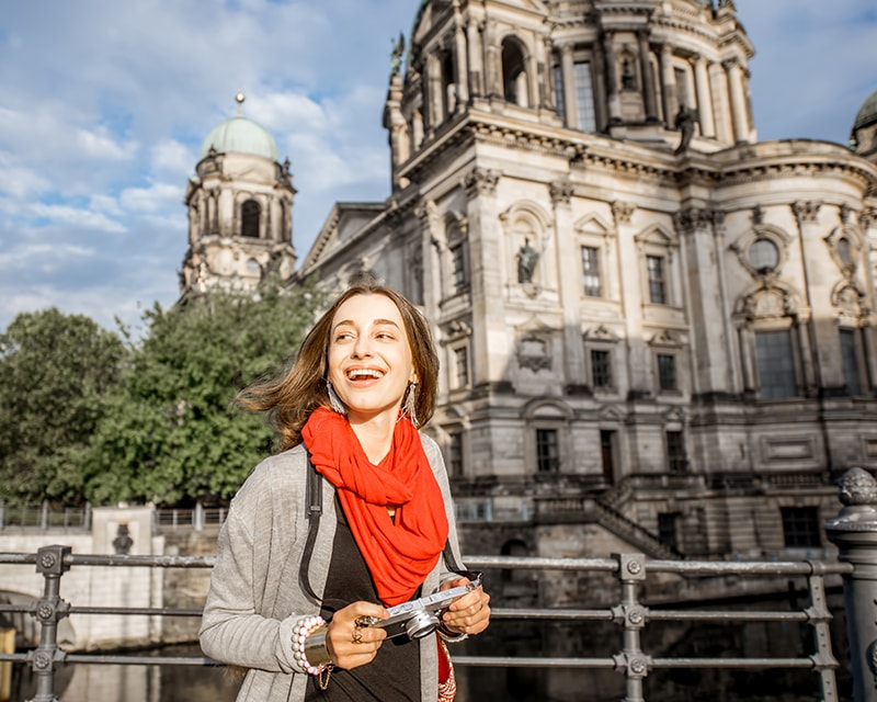 Student in Germany laughing and holding a camera outside a historic building. 