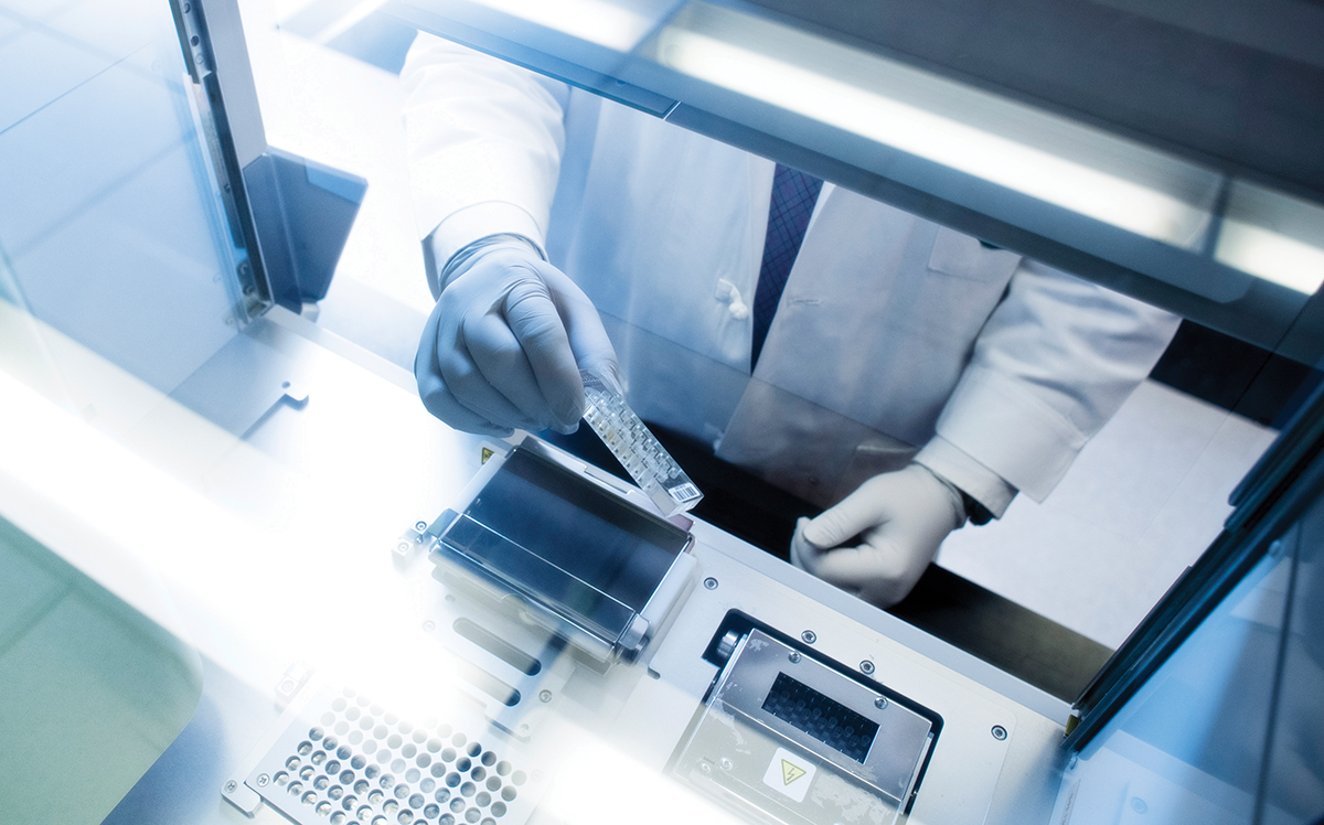 Image of a person in a white coat and latex gloves conducting an experiment in one of UAB's labs. 
