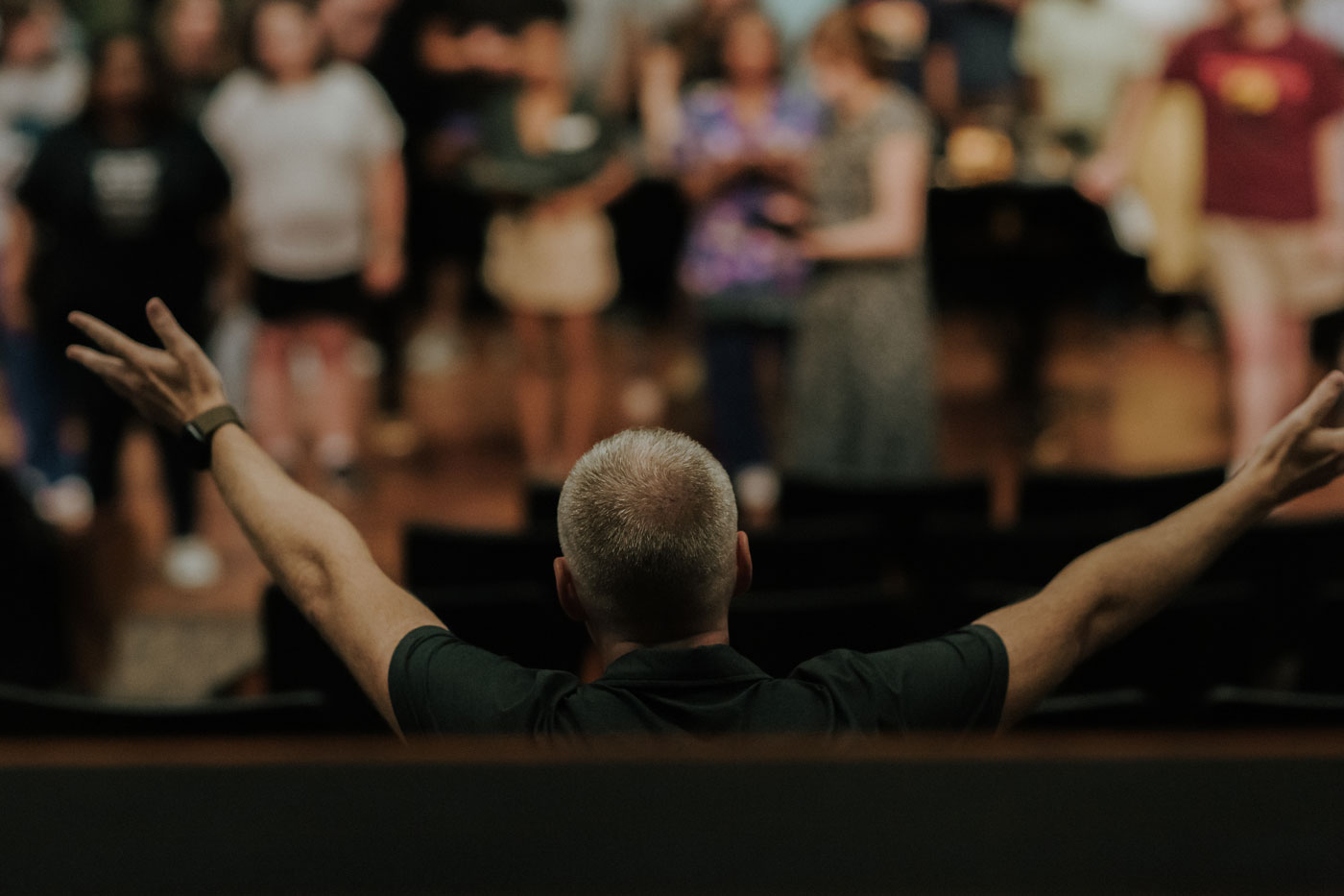 The conductor with his hands spread wide, the choir out of focus in the background.