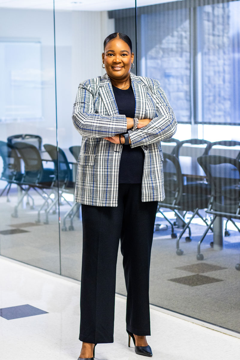 Tatum stands with arms crossed in front of a glass-walled meeting room, smiling confidently.