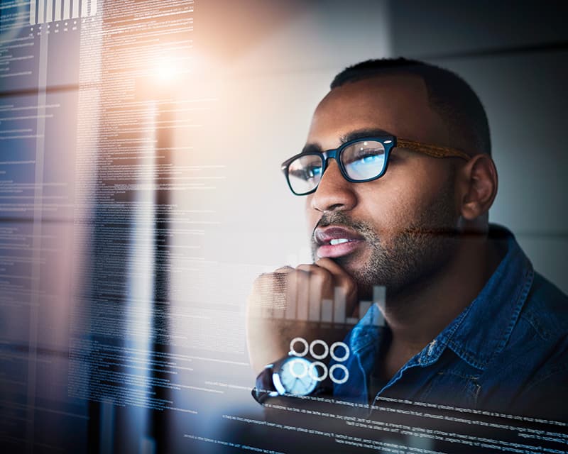 Black male in glasses with his chin on one hand, seen through data being displayed on a clear board.