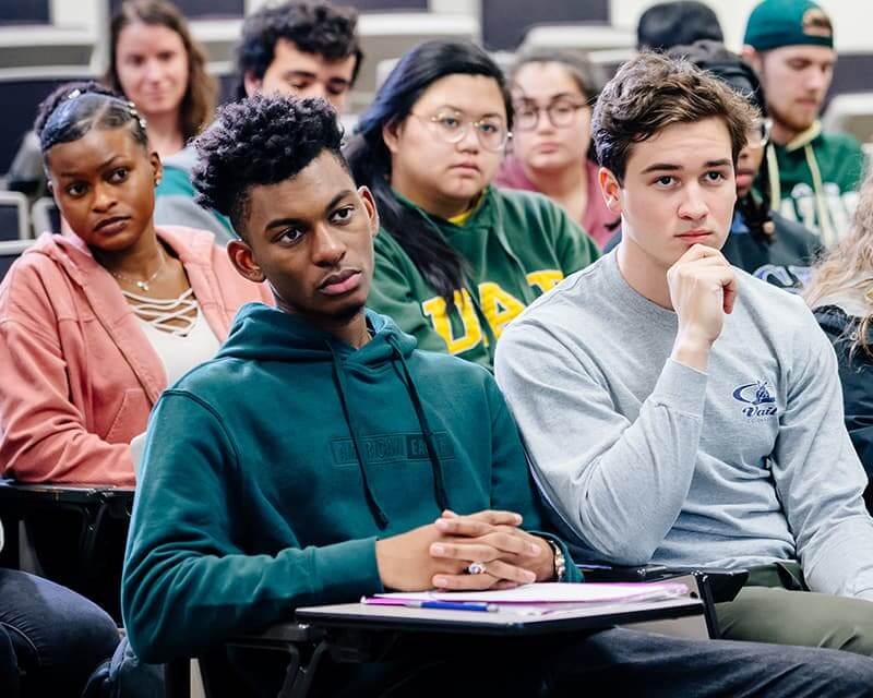 Students in a class of various genders and races, a black male and white male in foreground. 