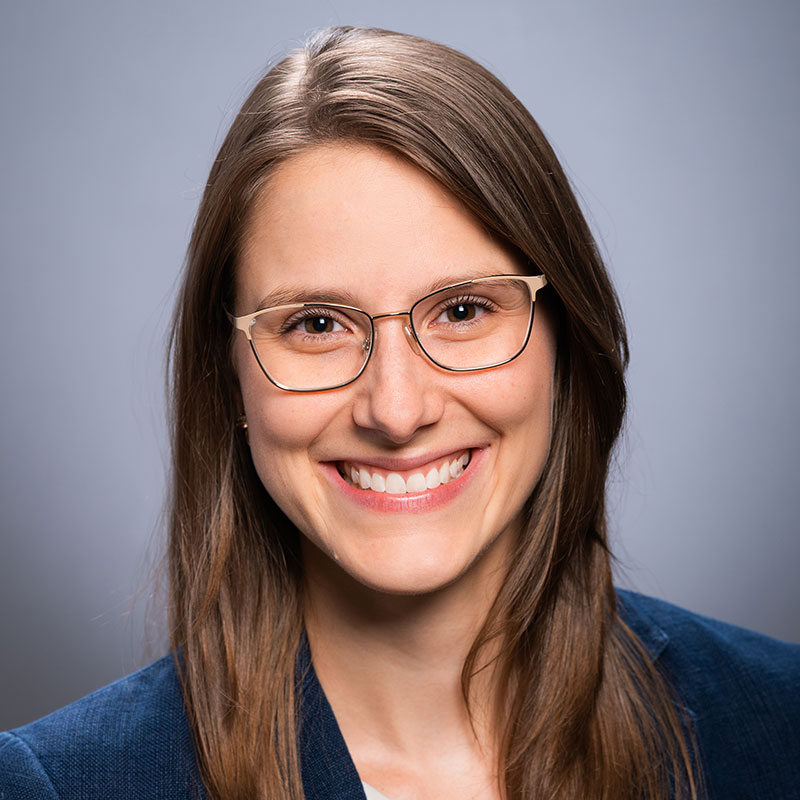 Caroline Richter has long brown hair and is wearing tan-colored cat-eye glasses and a navy blazer.