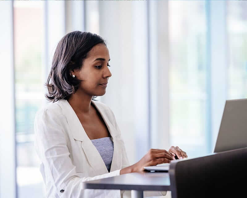 A woman working on her laptop in a glass-walled office. 