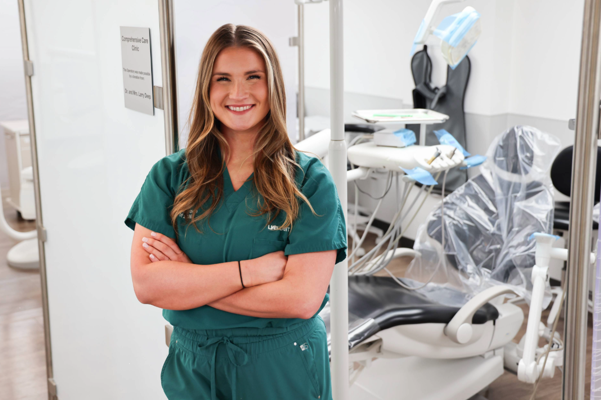 Baleigh Robertson standing with arms crossed and smiling in front of clinic operatory in a UAB dental clinic at the UAB School of Dentistry.