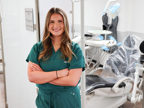 Baleigh Robertson standing with arms crossed and smiling in front of clinic operatory in a UAB dental clinic at the UAB School of Dentistry.