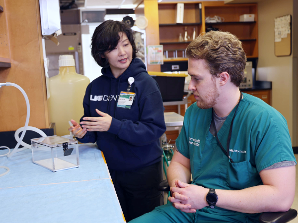 Dr. Cheon standing and talking to Warren Smith (sitting) about her lab in the School of Dentistry dental research lab.