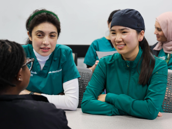 Two women in green scrubs smiling at person across from them over a table