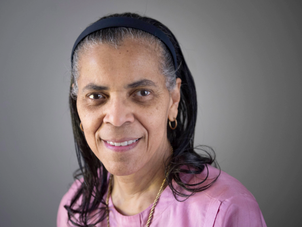 Woman in pink shirt and black hair smiling in front of gray background