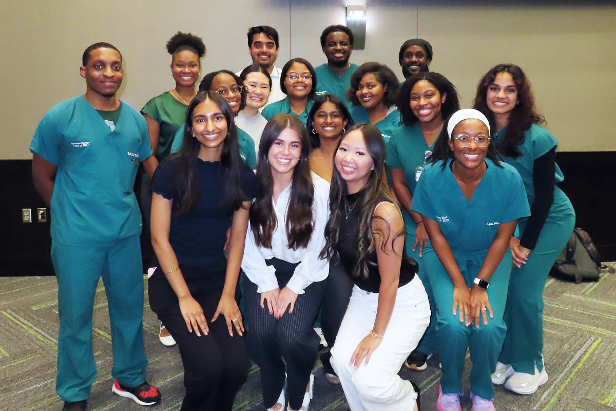Group photo of men and women wearing professional attire and green scrubs in a conference setting