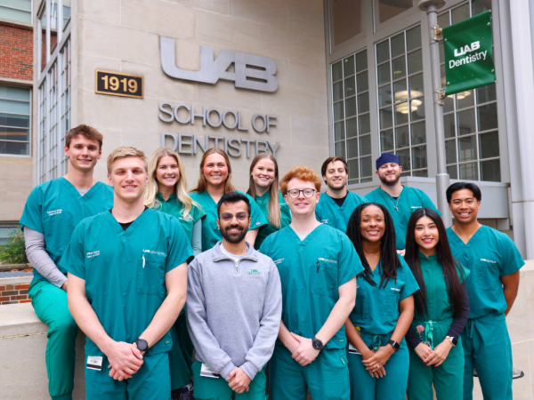 Group of dental students smiling for photo in front of UAB School of Dentistry