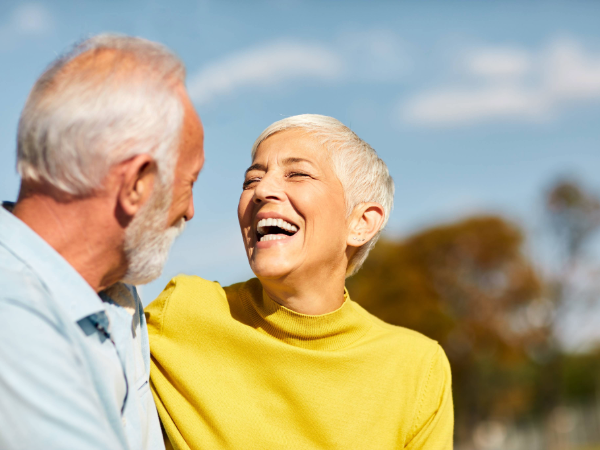 A senior couple smiling at each other in an outdoors setting