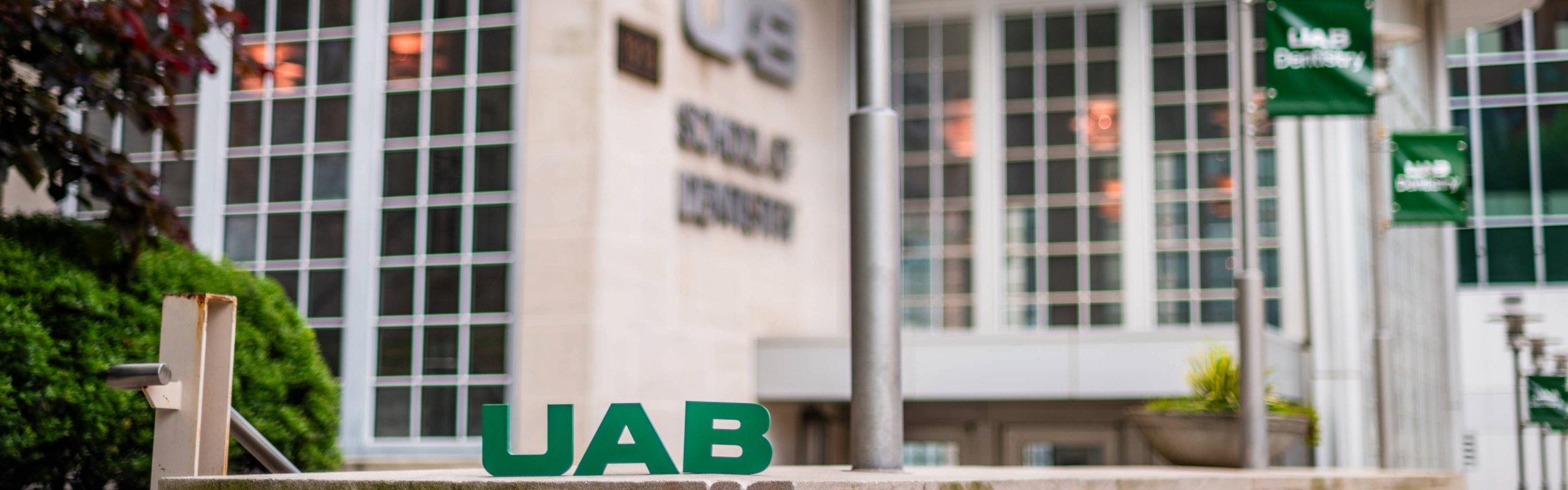 Image of UAB School of Dentistry exterior with green UAB block letters sitting on concrete wall