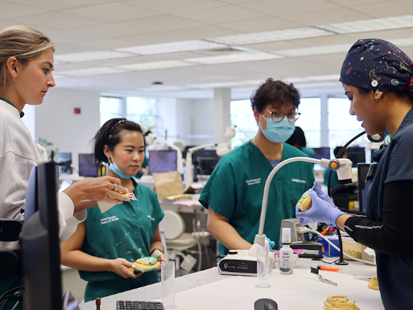Three dental students watching faculty member while holding dental models in the preclinical dentistry lab