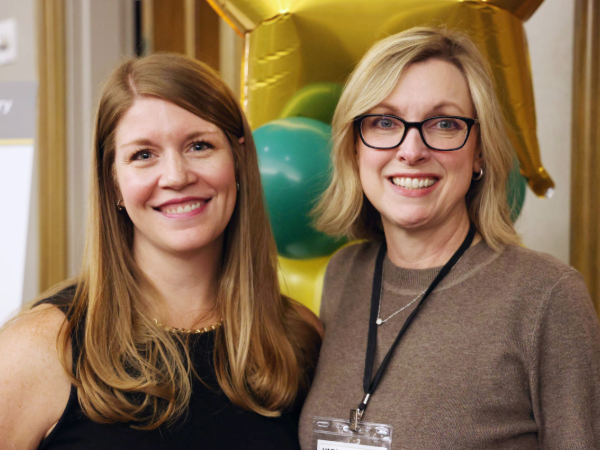 Ann MArie Karaki and Rachel Anne Steadham smiling for photo in front of celebratory balloons