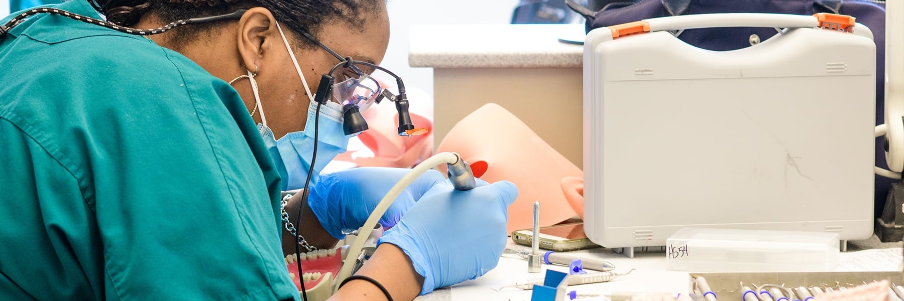 Woman wearing a mask working on a mold of teeth.