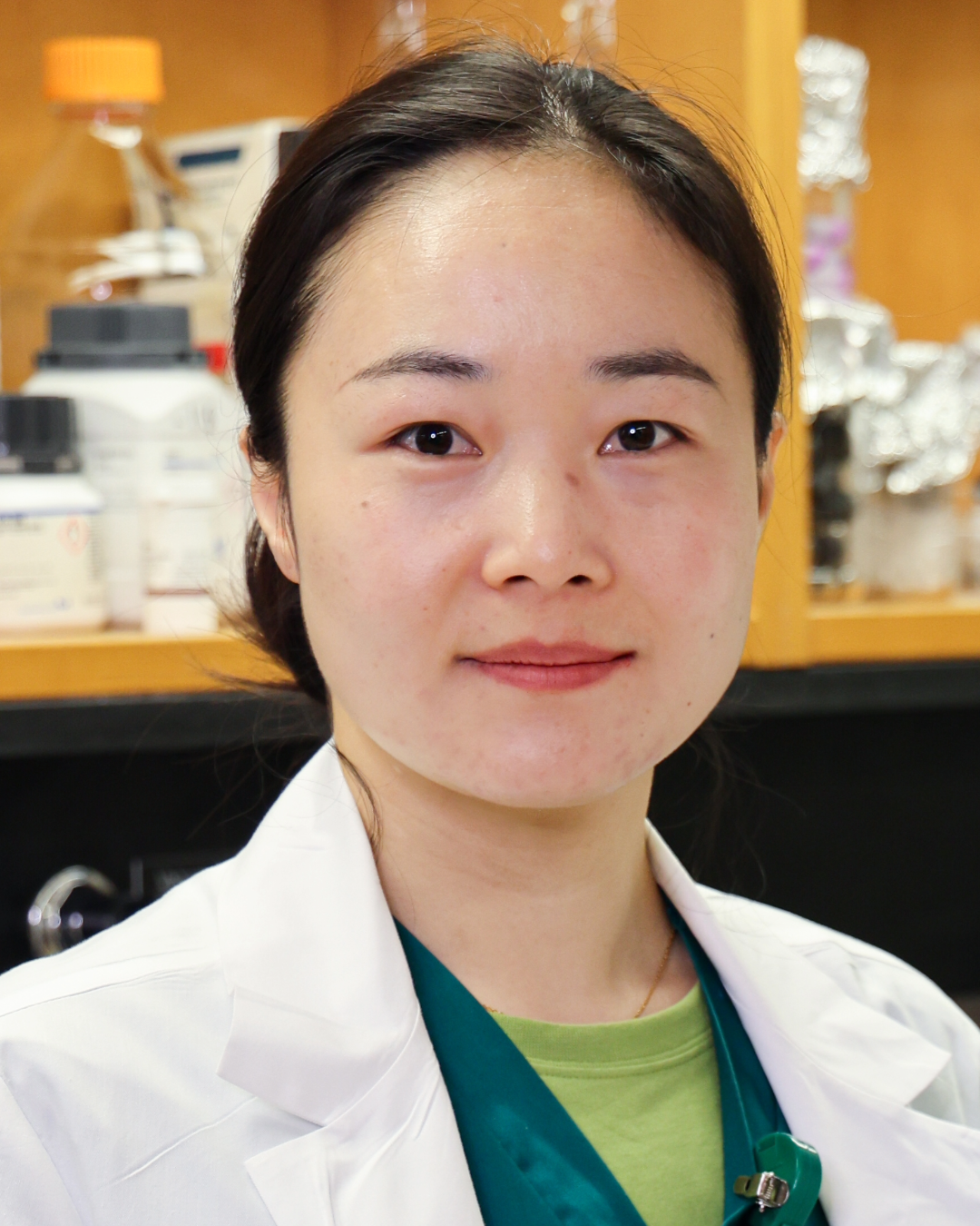 Woman with black hair and white lab coat smiling in lab setting