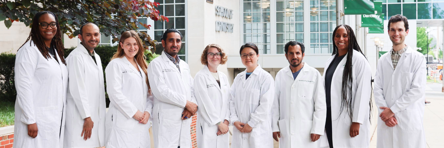 A group of DART trainees in white lab coats standing together outside a campus building.