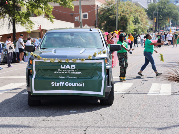Truck with SOD Staff Council banner driving through UAB Homecoming Parade with members passing out flyers beside it