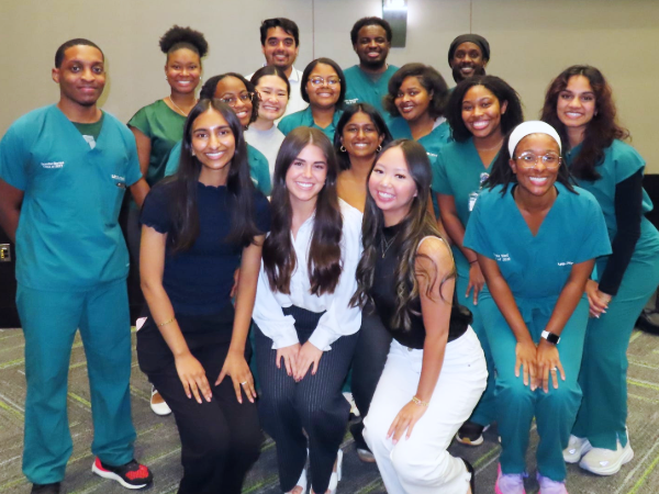 Group photo of men and women wearing professional attire and green scrubs in a conference setting