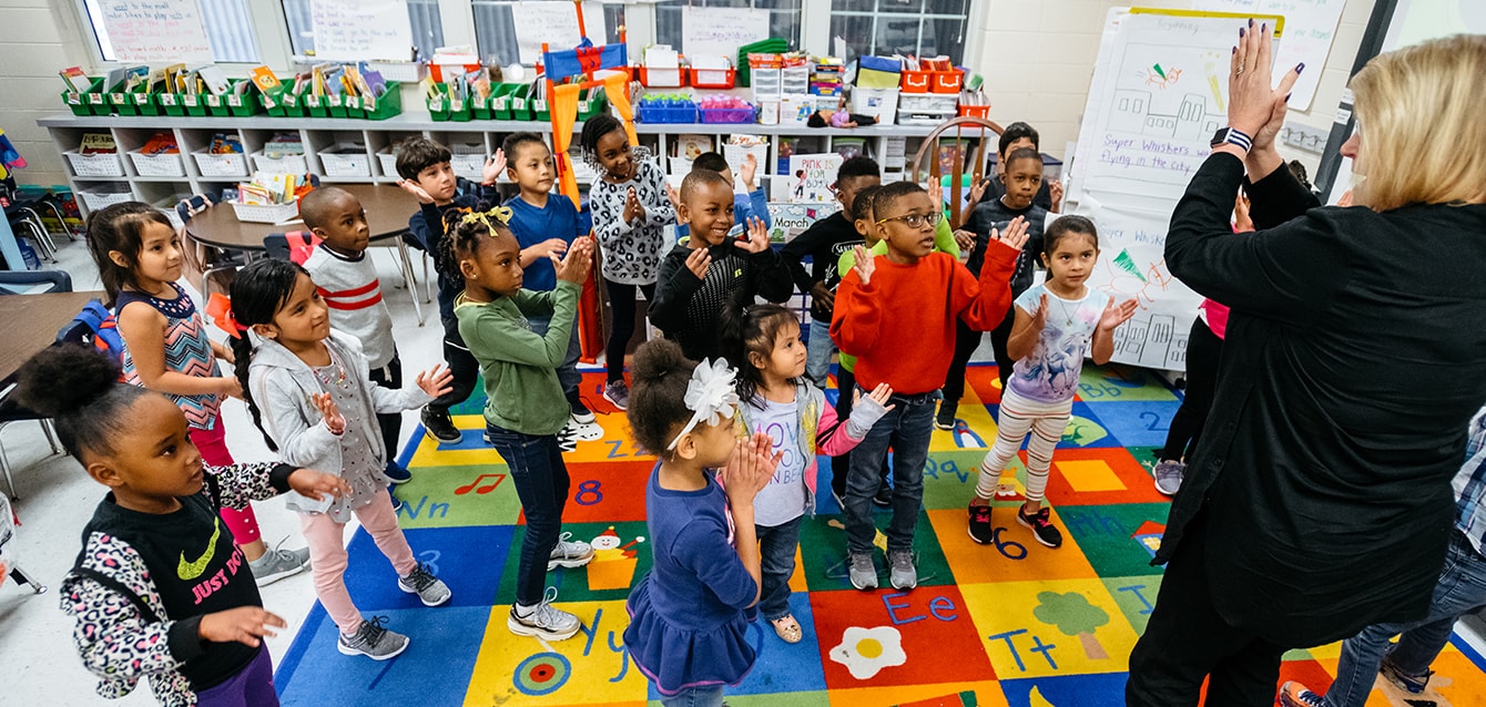 A teacher in a colorful classroom leads a group of elementary school children in an activity. 