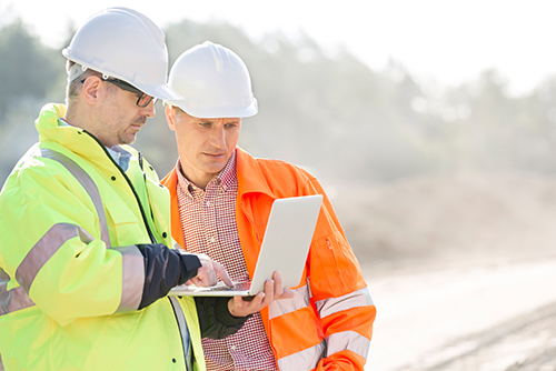Men in hardhats looking at a laptop at a construction site.