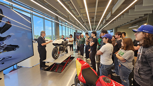 A guide speaks to a group of students in front of a motorcycle museum exhibit