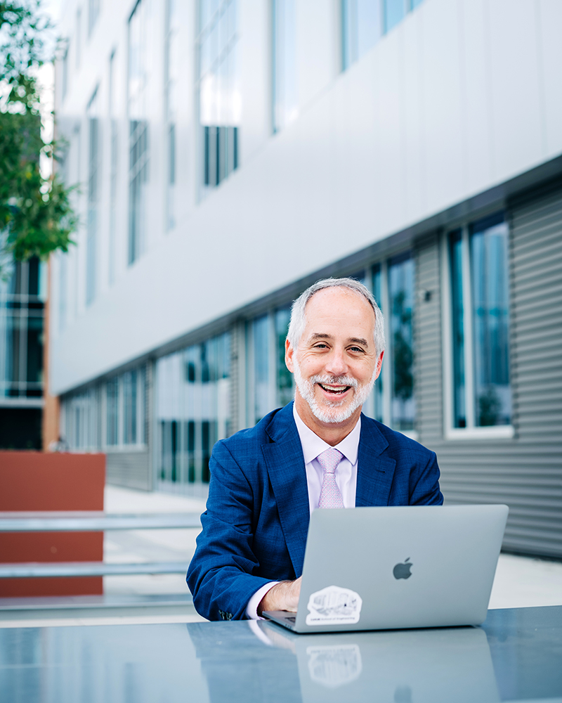 Engineering dean seated with a laptop in the courtyard of the Science and Engineering Complex.