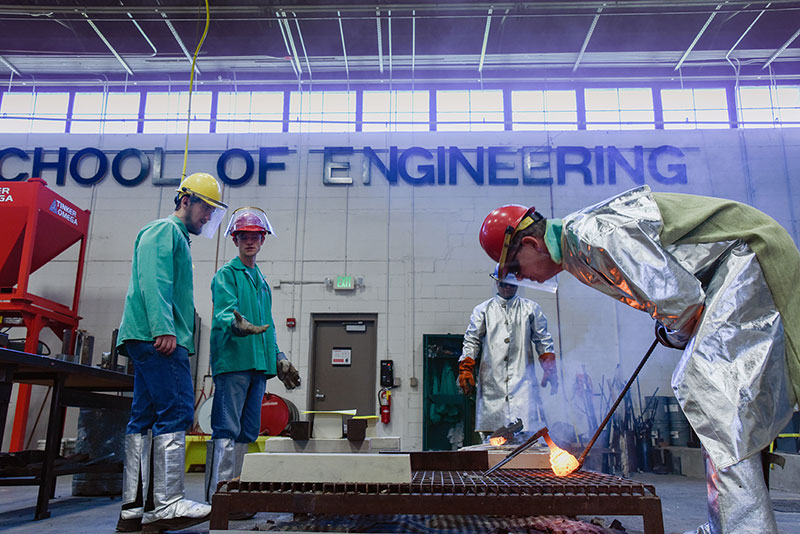 Students in safety clothes working in a lab under large painted words "School of Engineering."