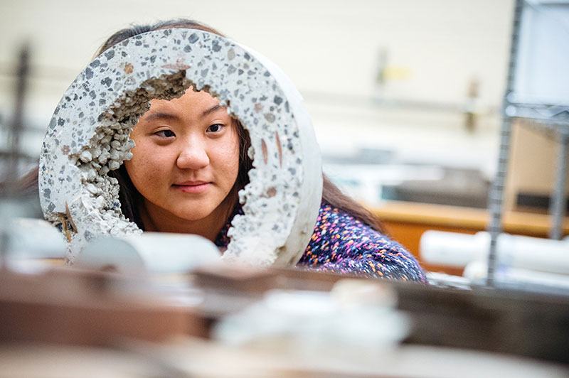 A female Civil Engineering student peering through a concrete cylinder. 