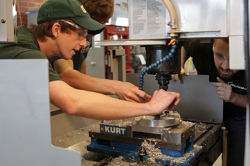 A mechanical engineering student in the lab, supervised by a lab manager. 