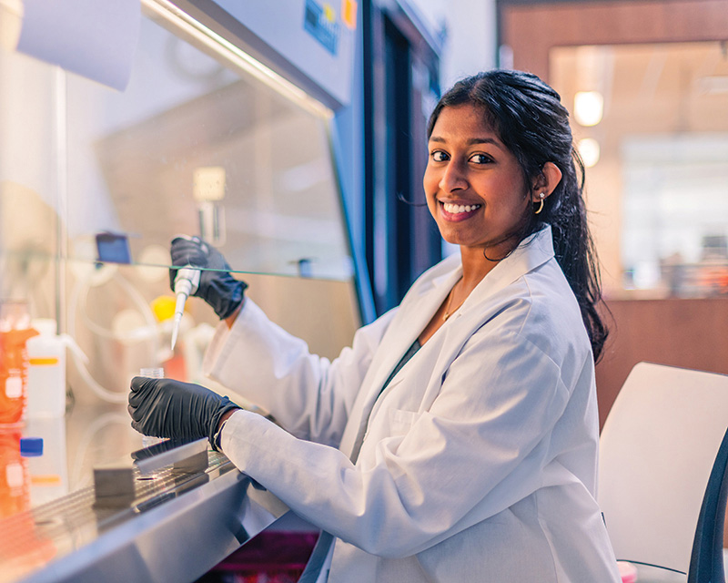 Female student sits at a lab bench pipetting material into a vial.