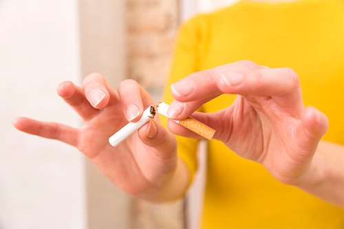 Close-up photo of a woman in a yellow shirt snapping a cigarette in half