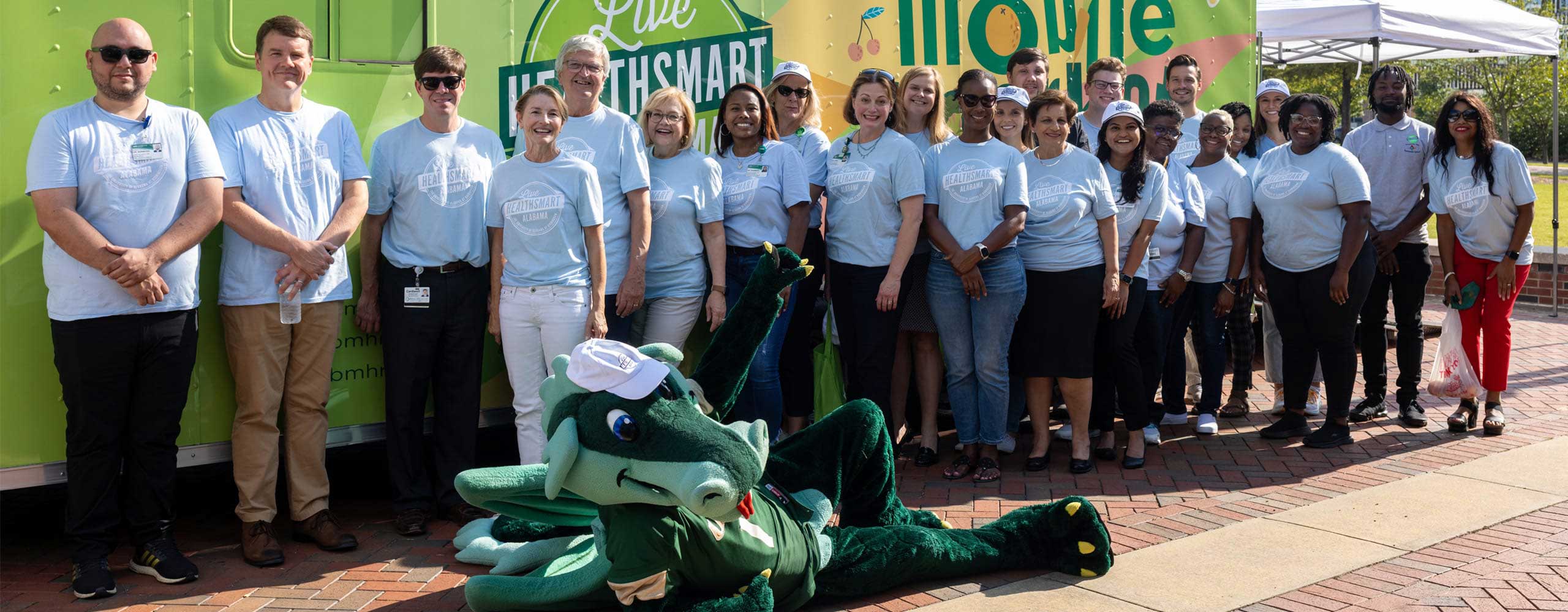 Members of Live Healthsmart pose outside one of the buses with UAB mascot Blaze.