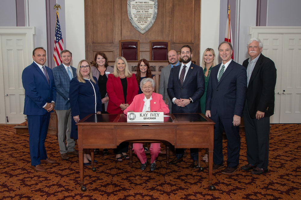 Gov. Kay Ivey signs the bill. Alabama AHEC Associate Director and UAB Family and Community Medicine Assistant Professor Becky Reamey looked on, third from left in the second row.
